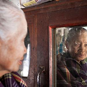 An elderly woman looks in the mirror in Myanmar