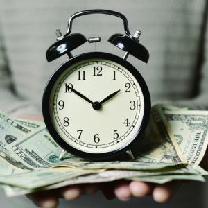 Hands holding money and an alarm clock